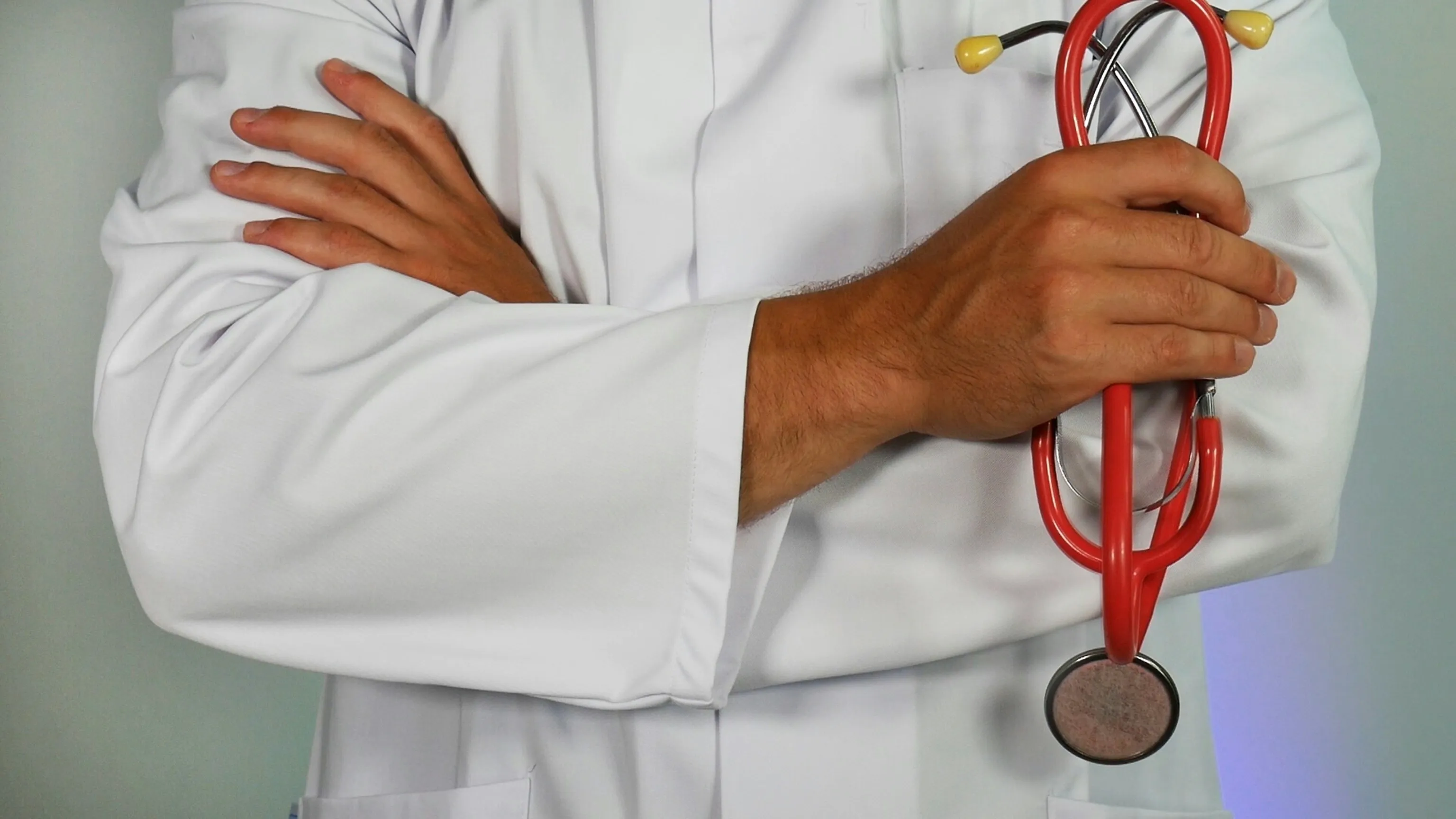 Clinician in a white coat holding a stethoscope, arms crossed.