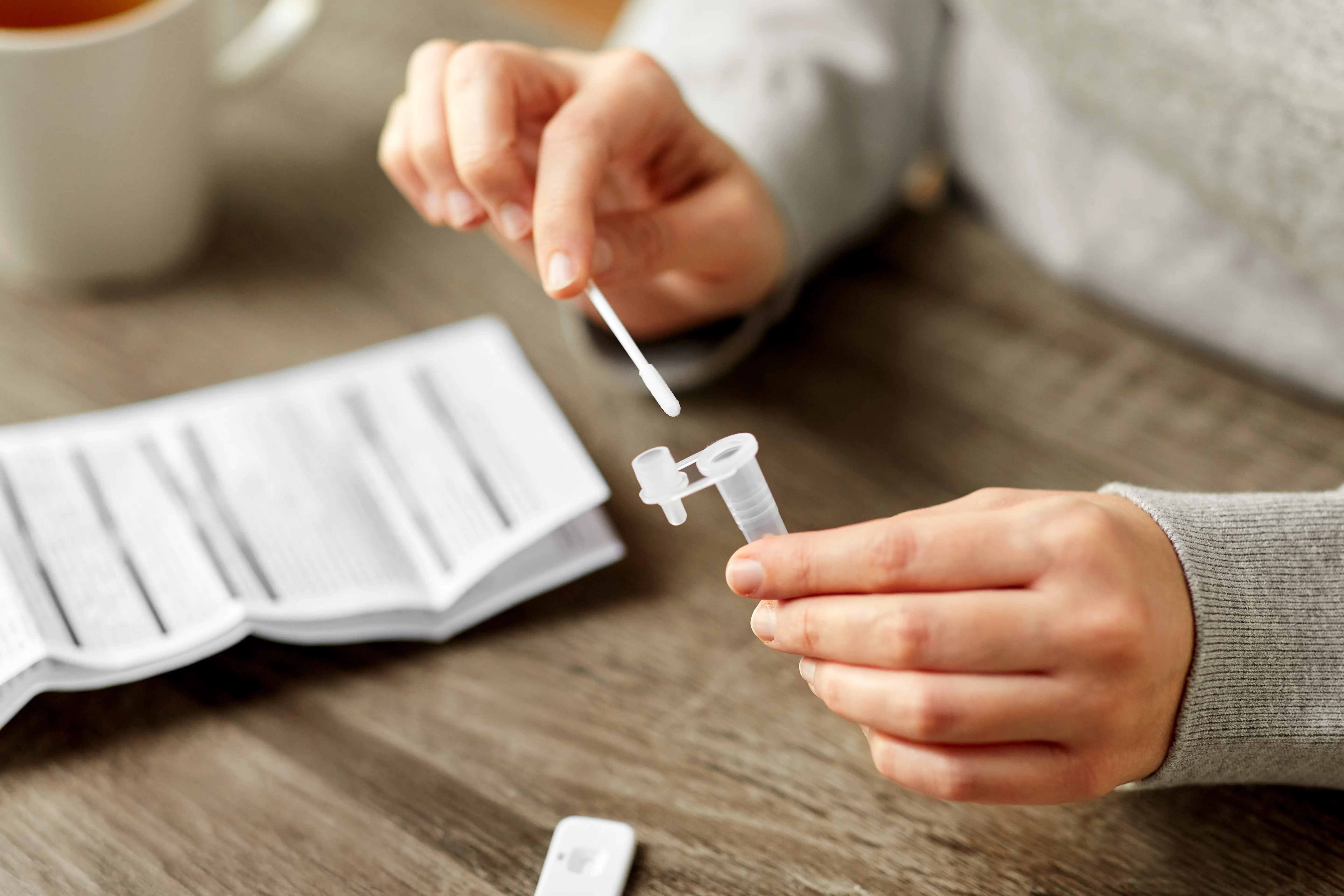 Hands transferring a swab sample into an extraction tube beside a rapid test and instructions.
